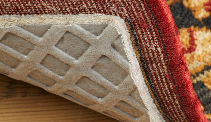 a close-up view of a corner of a rug lifted to reveal a rug pad underneath