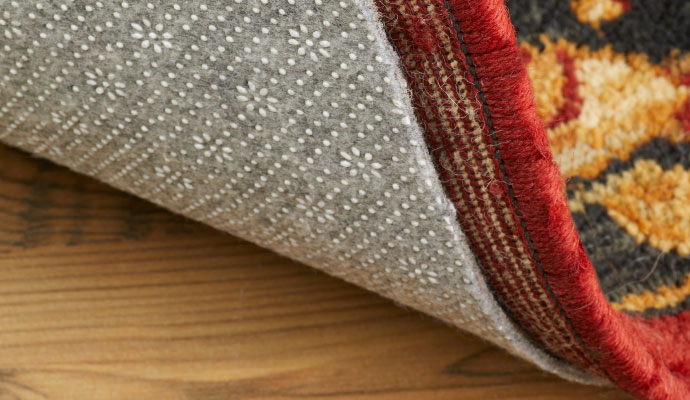 Close-up view of a rug corner lifted to reveal a non-slip rug pad underneath