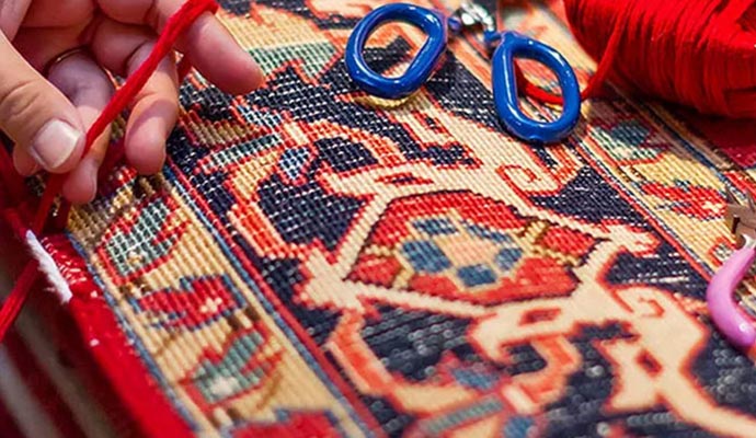 A person is repairing the binding of a rug using a needle threaded 